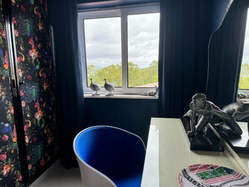 une chambre bleue avec une table et deux oiseaux dans une fenêtre dans l'établissement Palm View Guesthouse, adults only, à Luz