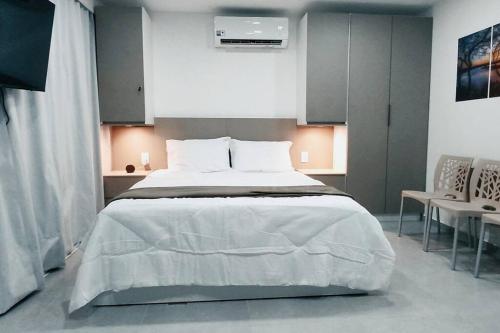 1 dormitorio con 1 cama blanca grande y 2 sillas en Flat 305 Porto Prime com Rooftop e Piscina, en Porto de Galinhas