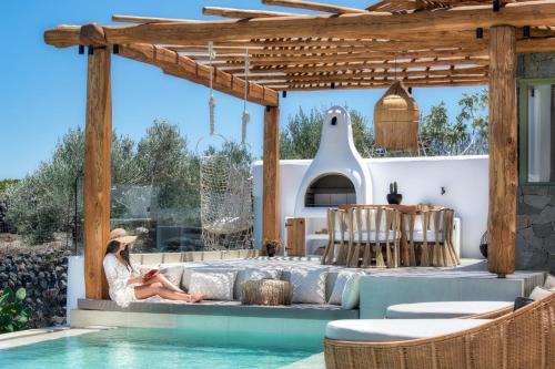 a woman sitting on a couch under a pergola by a pool at Ayama Hideaway Private Villa in Fira