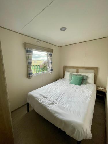 a bedroom with a large white bed with a window at Caravan at Seawick Holiday Park Close to Beach in Saint Osyth