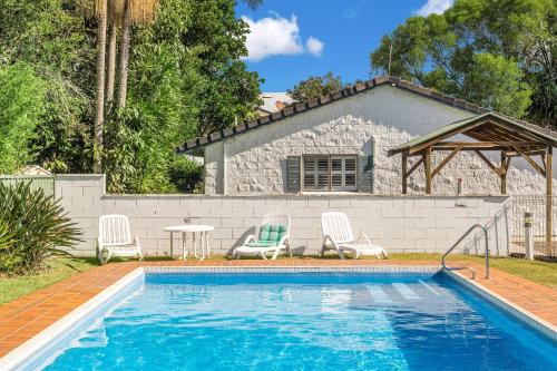a swimming pool with chairs and a table and a house at Iluka Villa 10 in Iluka