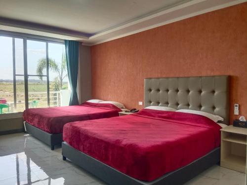 a bedroom with two beds with red sheets and a window at Blue Hotel and Resort in Porac