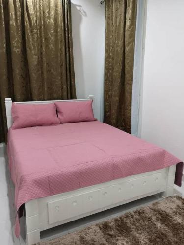 Cama en habitación con manta rosa y cortinas en Inapsinggah homestay, en Kota Bharu