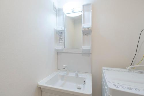 a white bathroom with a sink and a mirror at Curasion Oyodonaka in Osaka