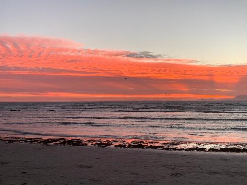 a sunset over the ocean with a sandy beach at Seaview on 2822 Happy Whale Cottage in Bettyʼs Bay