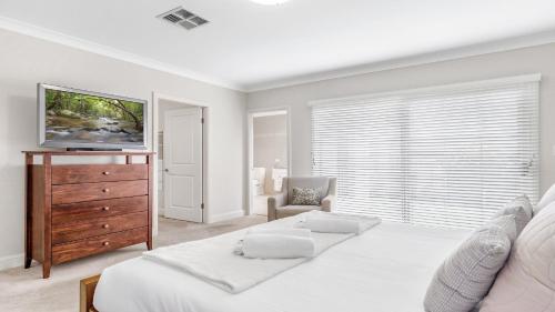 a white bedroom with a bed and a dresser with a television at La Vita - The Vintage in Pokolbin