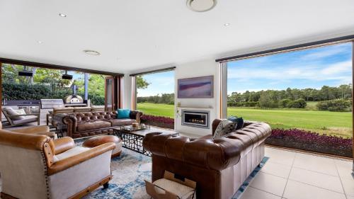 a living room with leather furniture and large windows at Peppertree Ponds in Pokolbin