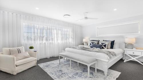 a white bedroom with a large bed and a chair at Montauk House in Pokolbin