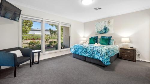 a bedroom with a bed and a chair and windows at Cypress Point Lodge - The Vintage in Pokolbin