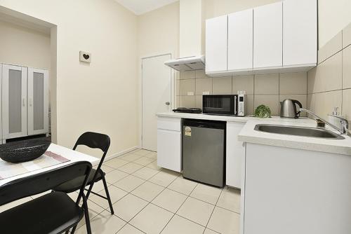 een keuken met witte kasten, een wastafel en een magnetron bij 51CR3 - Lovely One Bedroom Apt Next to RMIT! AC, 50incTV in Melbourne