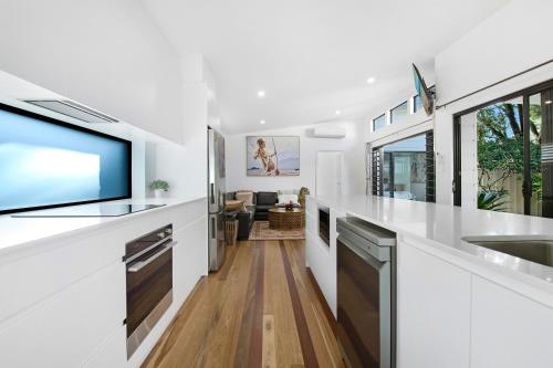 a kitchen with white countertops and a large tv at Elvis on Brodie - 2025 TRAVELLER AWARD WINNER in Coffs Harbour
