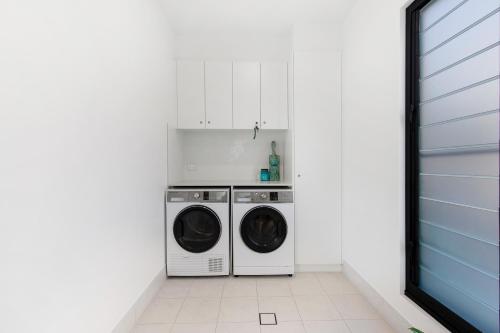 a white laundry room with a washer and dryer at Elvis on Brodie - 2025 TRAVELLER AWARD WINNER in Coffs Harbour
