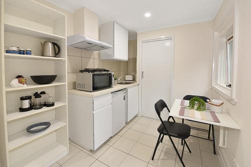 - une cuisine blanche avec une table et un four micro-ondes dans l'établissement Lovely One Bedroom Apt Next to RMIT! AC, 50inc TV, à Melbourne