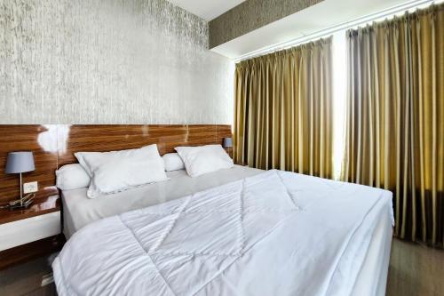 une chambre avec un grand lit blanc et une fenêtre dans l'établissement RedLiving Apartemen Grand Kamala Lagoon by Ownr Room, à Pekayon Satu