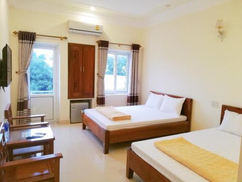 a bedroom with two beds and a table and two windows at Thành Đạt Hotel in Cửa Lô