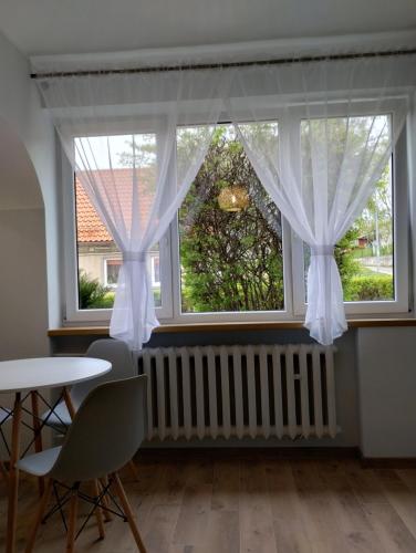 2 Fenster mit weißen Vorhängen sowie einem Tisch und Stühlen in der Unterkunft Apartament na Mazurach -Ryn in Ryn