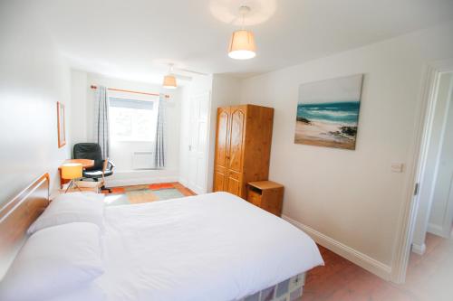 a white bedroom with a large bed and a chair at Seacliff HH No 4 in Dunmore East