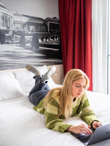 a woman laying on a bed using a laptop at B&B HOTEL Brussels Centre Gare du Midi in Brussels