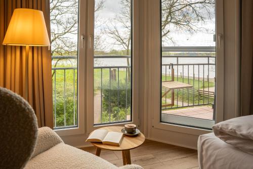 Zimmer mit großen Fenstern und einem Tisch mit einem Buch in der Unterkunft Hotel Seeblick in Thülsfeld