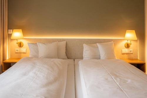 2 bedden in een hotelkamer met witte lakens en kussens bij Hotel Seeblick in Thülsfeld