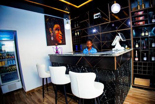 a woman standing at a bar with white chairs at Vic & J Lounge and Hotel Asaba in Asaba