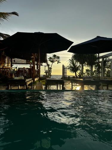 a swimming pool with umbrellas and tables and the ocean at White Sand Villa - Beach front in Hikkaduwa