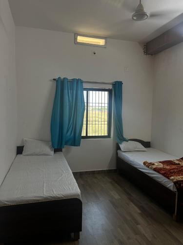 Habitación con 2 camas y ventana con cortinas azules. en Marina Home Stay en Bodh Gaya