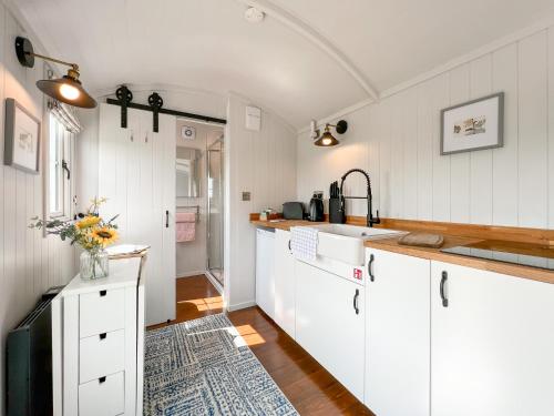 una cocina con armarios blancos y fregadero en Farm Shepherd's Hut, en Wendron