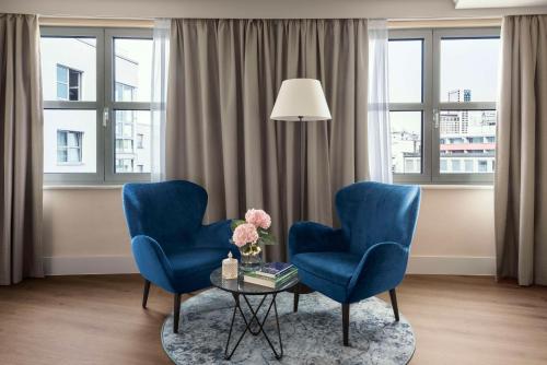 ベルリンにあるNH ベルリン クアフュルステンダムの窓のある客室で、青い椅子2脚とテーブル1台が備わります。