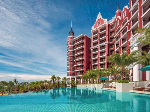 een zwembad voor een groot rood gebouw bij Mövenpick Resort Phan Thiet in Phan Thiet