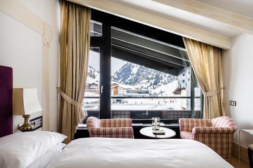 une chambre d'hôtel avec un lit, deux chaises et une fenêtre dans l'établissement A-ROSA Collection Hotel Thurnher's Alpenhof, à Zürs