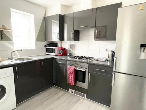eine Küche mit schwarzen Schränken und einem Kühlschrank aus Edelstahl in der Unterkunft Crescent Apartment - Two bedroom in Goodmayes