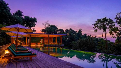 a resort with a pool and a deck with chairs and an umbrella at Sanglung Villas & Suites in Kubutambahan