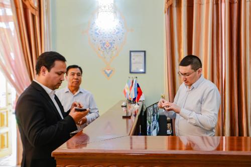 three men standing at a desk looking at their cell phones at Yangi Sharq in Samarkand