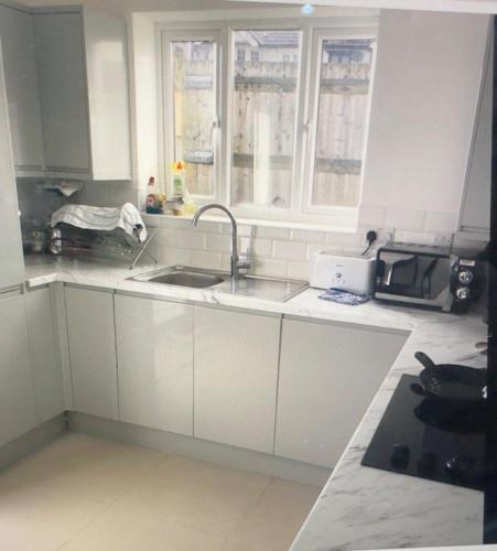 a kitchen with white cabinets and a sink and a window at Ian house abbeywood in Abbey Wood