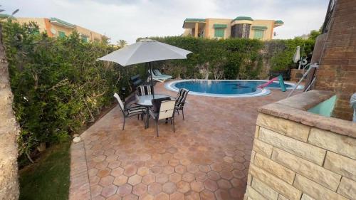 una mesa con sillas y una sombrilla junto a la piscina en Villa123, en El Alamein