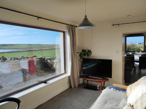 a living room with a large window and a television at Castlehill, Sanday in Sanday