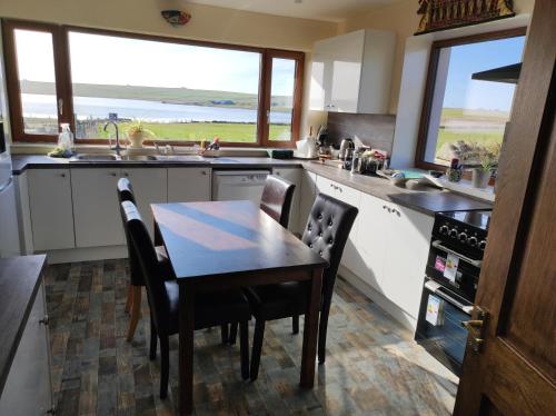 a kitchen with a table and chairs and windows at Castlehill, Sanday in Sanday