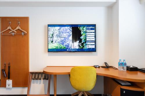 a desk with a yellow chair and a television on a wall at Sun Days Kagoshima in Kagoshima