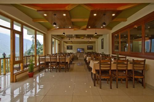 un comedor con mesas, sillas y ventanas en Goroomgo Hotel BD Resort Manali - Excellent Stay with Family, Parking Facilities en Manāli