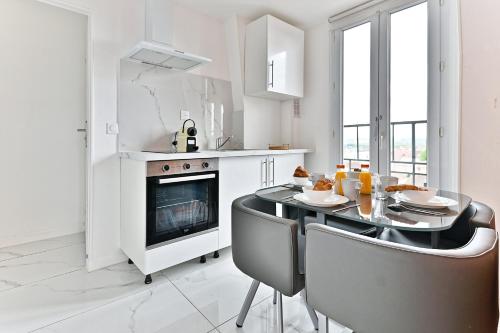 - une cuisine blanche avec une table à manger et des chaises dans l'établissement Appartement paisible en banlieue parisienne, à Gagny
