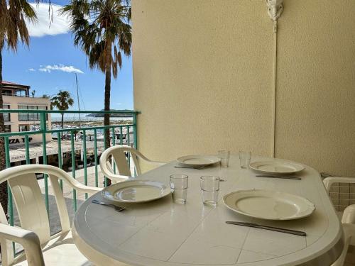 une table blanche avec des assiettes et des verres sur un balcon dans l'établissement Appartement 2 pièces avec terrasse et parking à 150m de la mer - FR-1-225-451, à Argelès-sur-Mer