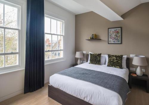 a bedroom with a large bed and two windows at Wells Court by Aeria Apartments in London