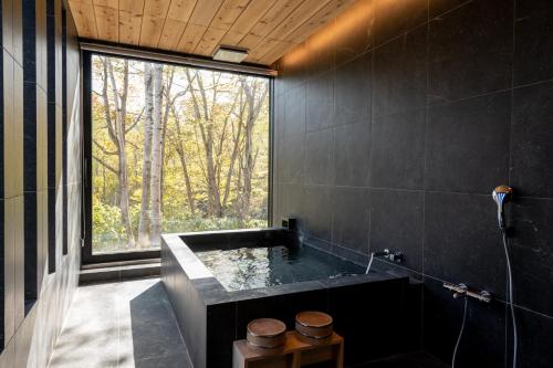 La salle de bains noire est pourvue d'une baignoire et d'une grande fenêtre. dans l'établissement Yuki Sugi at Intuition, à Niseko