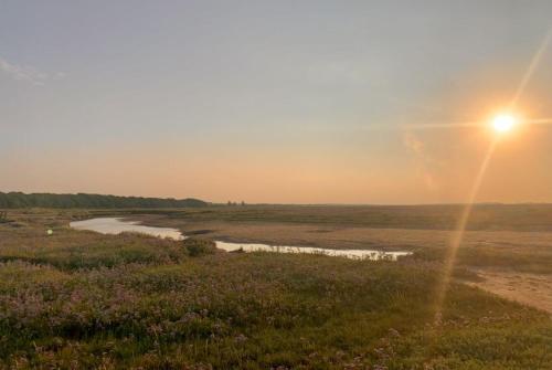 a sun setting over a field with a river at Saltmarsh Hut in Stiffkey