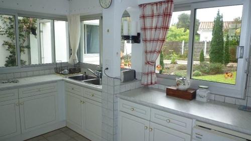 La cuisine est équipée de placards blancs, d'un évier et de fenêtres. dans l'établissement La Villa de la foret, à Saint-Hilaire-de-Riez