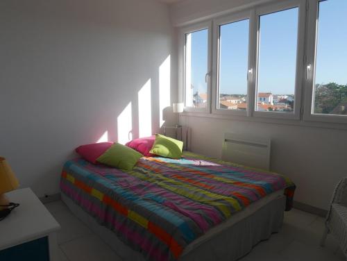 Schlafzimmer mit einem Bett mit bunter Bettwäsche und Fenstern in der Unterkunft L'estivant sur l'océan in Saint-Hilaire-de-Riez
