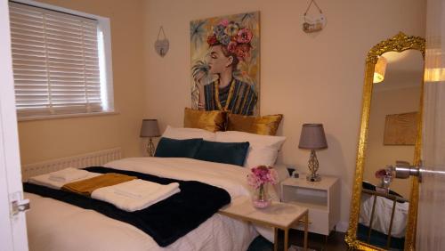 Milton Keynes 3 Bed House في Shenley Church End: غرفة نوم بسرير ومرآة ولوحة
