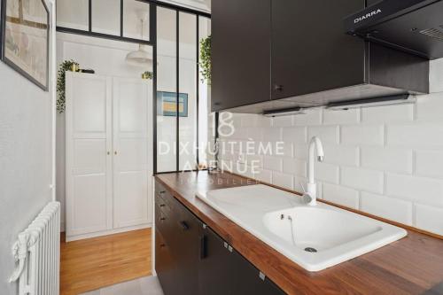 - une cuisine avec un évier blanc et des placards noirs dans l'établissement Modernité et confort à Montmartre, à Paris