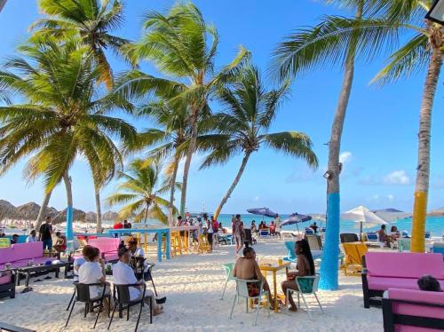 personas sentadas en mesas en una playa con palmeras en Hostal Las Rosas de Punta Cana en Punta Cana